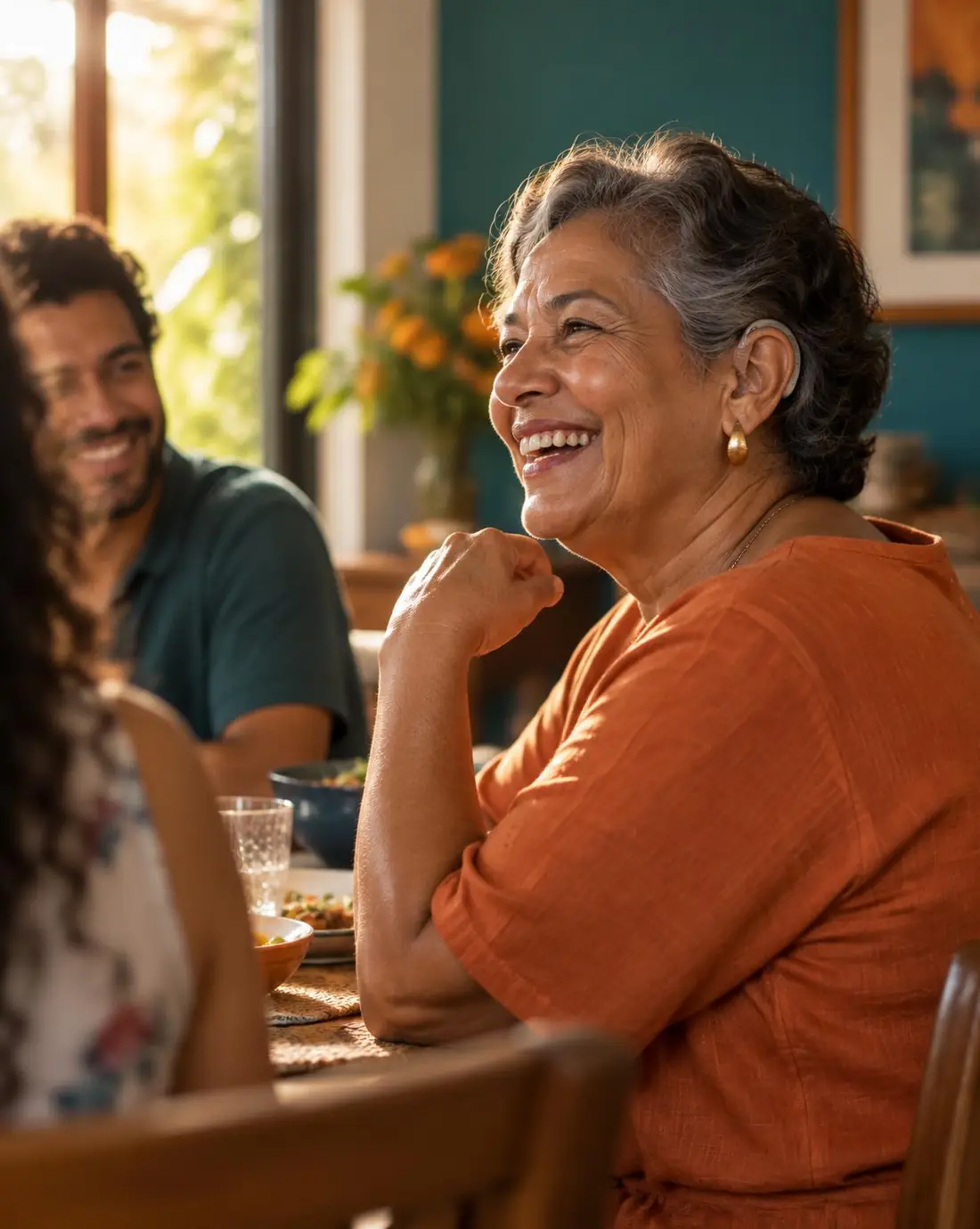 Mulher sorrindo durante uma conversa em família, usando aparelho auditivo